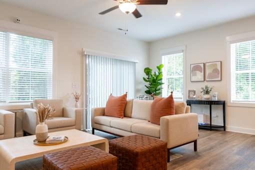 A living room with a white sofa, a brown ottoman, and a white coffee table.