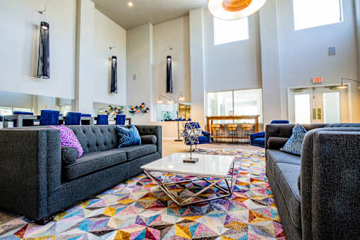 A large room with a grey couch and a colorful rug.