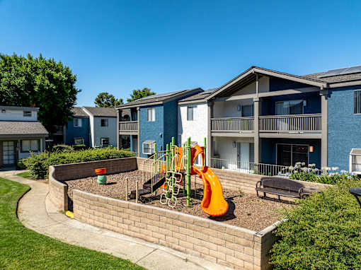 A playground area with a slide and a bench in front of townhomes.