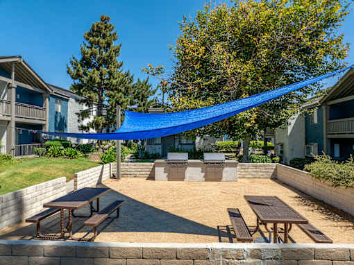 An outdoor patio space with grills and picnic tables with a blue overhang.