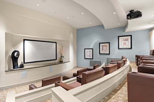 A room with a row of brown leather chairs facing a television.