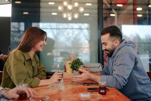 A man and a woman are sitting at a table in a restaurant, enjoying a meal and drinks together.