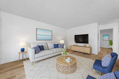 A living room with a white couch, blue chairs, and a painting on the wall.