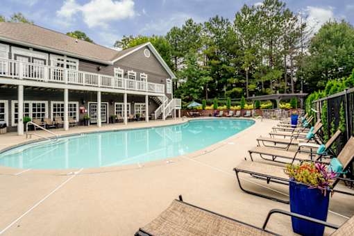 A pool area with a building and lounge chairs.