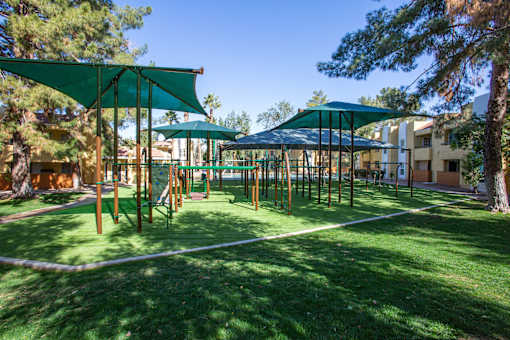 A playground with a green canopy and a white rope fence.