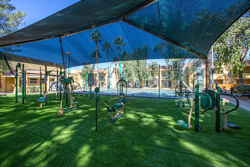 A playground with a green canopy and a variety of equipment.