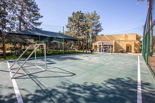 A tennis court with a green fence and a building in the background.