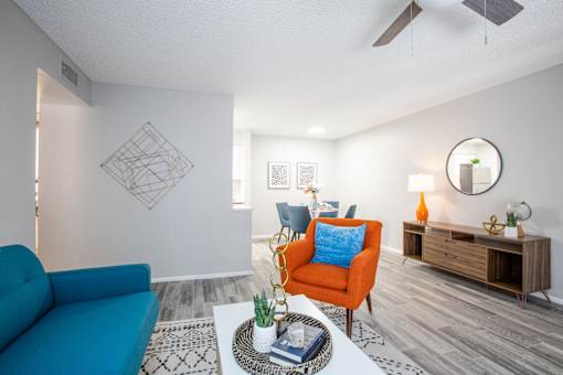 A living room with a blue couch, a red chair, and a round mirror on the wall.