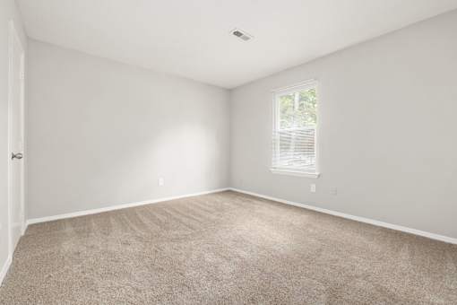 A room with a carpeted floor and a window with blinds.