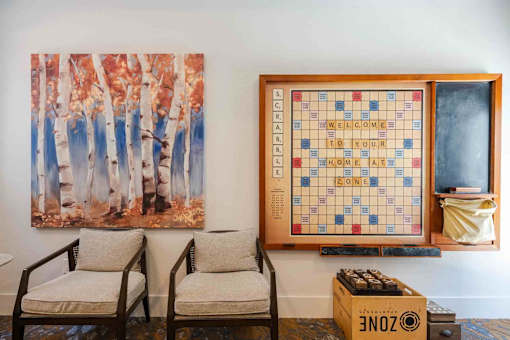 A game of Scrabble is set up on a wall next to a painting of trees.