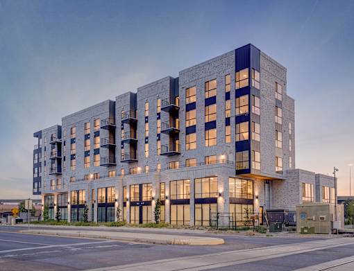 A modern multi-story building with balconies is illuminated from within.