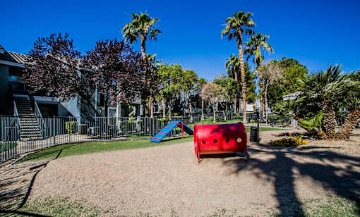 A playground with a red slide and a blue slide in the middle of a sandy area.