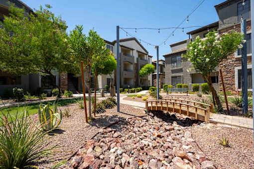 A small bridge crosses a rocky area in front of apartment buildings.