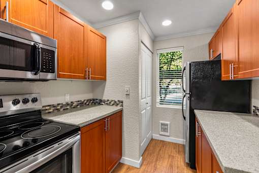 Galley kitchen with wood cabinets and modern appliances at Hubbard's Crossing Apartments, Kirkland, WA 98034