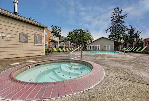 A hot tub sits in the middle of a concrete area with a building in the background.
