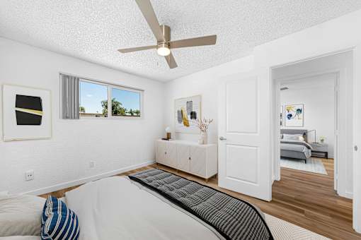 A bedroom with a bed, a ceiling fan, and a window with a view of the outdoors.