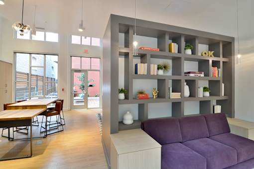 A modern living room with a purple couch and a grey bookshelf.