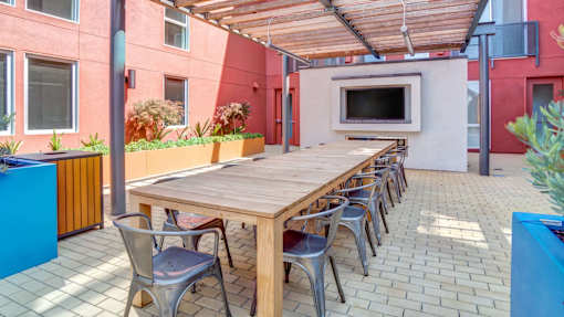 A long wooden table is surrounded by chairs on a patio.