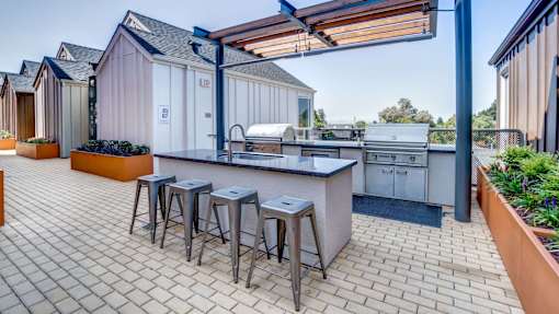 A patio with a bar and stools is surrounded by buildings.