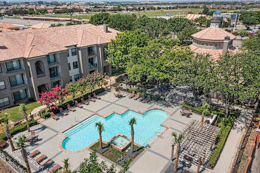 A swimming pool surrounded by palm trees and lounge chairs in front of a building.