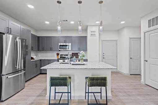 A modern kitchen with a marble island and two green chairs.