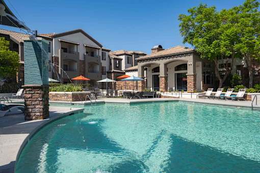 A swimming pool surrounded by lounge chairs and umbrellas in front of apartment buildings.