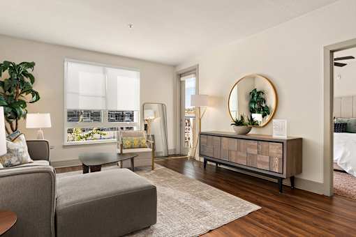 A living room with a grey sofa, a round mirror, and a wooden cabinet.