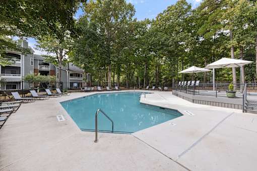 A swimming pool surrounded by trees and chairs.