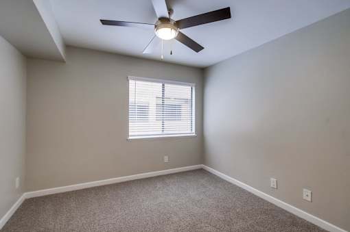 A room with a ceiling fan and a window with blinds.