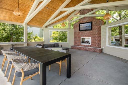 a covered patio with a large wooden table and chairs and a brick fireplace at Arbor Heights, Tigard, Oregon
