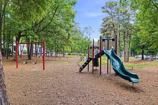 A playground with a green slide and a red swing set.