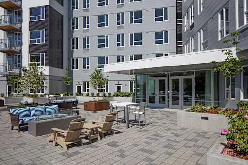 A patio with chairs and a table is surrounded by buildings.