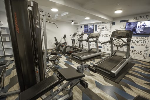 a gym with treadmills and other exercise equipment in a room with TV's on the wall