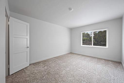 A room with a carpeted floor, a door, and a window showing trees outside at Hillsdale Garden Apartments, San Mateo, CA 94403