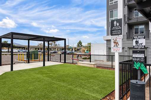 A dog waste station is located in a grassy area next to a parking lot.