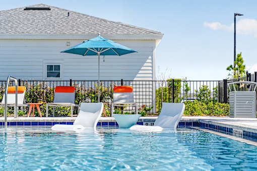 A pool with chairs and an umbrella in front of a house.