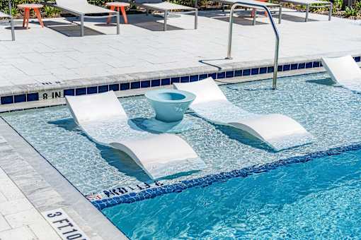 A pool with a blue tiled edge and white lounge chairs.