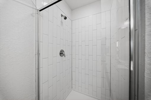 A white tiled shower stall with a glass door.