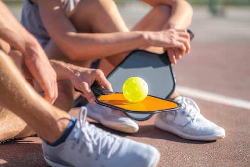 A tennis player is sitting on the ground with a racket and ball in hand.
