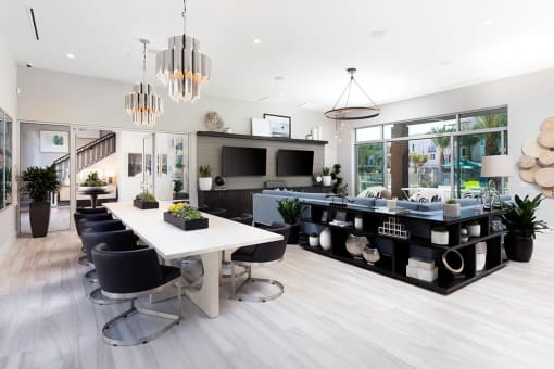 Clubroom area at Rivue apartments in Chula Vista San Diego with a long table and chairs and two TVs on the wall in front of a couch.