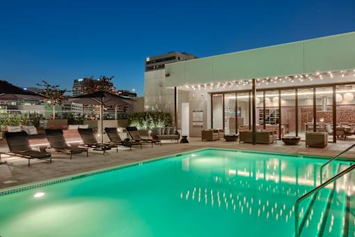 A pool in front of a building with lights on.