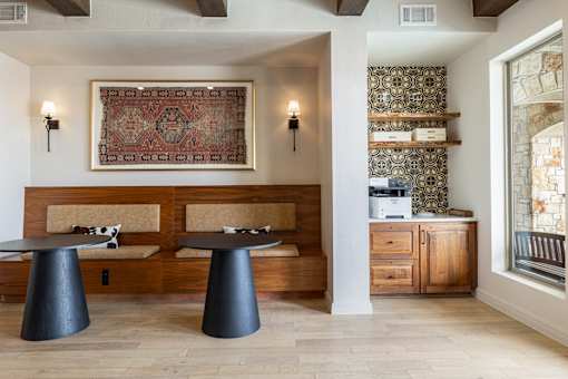 A room with a rug hanging on the wall and two tables in front of a bench.