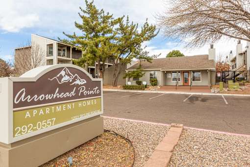 A brown and yellow sign for Arrowhead Pointe Apartment Homes sits in front of a parking lot.