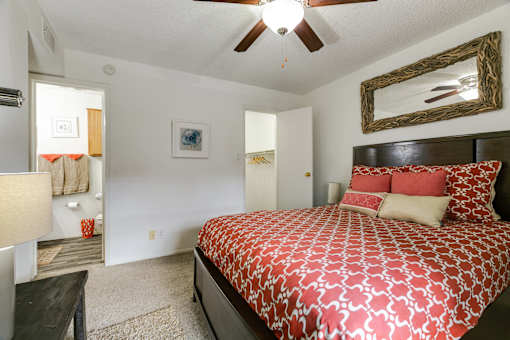 A bedroom with a patterned bedspread and a ceiling fan.
