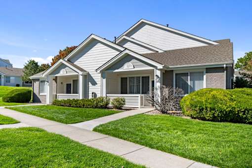 A house with a grey roof and white walls is surrounded by a well-kept lawn.