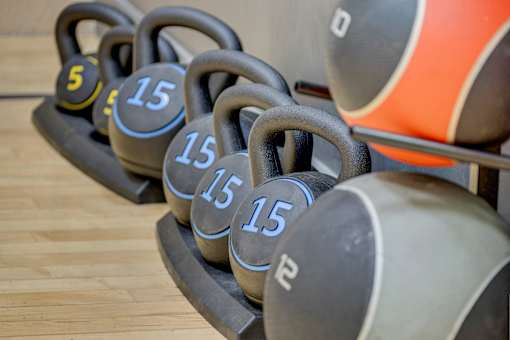 A set of kettlebells with weights of 5, 15, and 25 pounds are lined up on a wooden floor.
