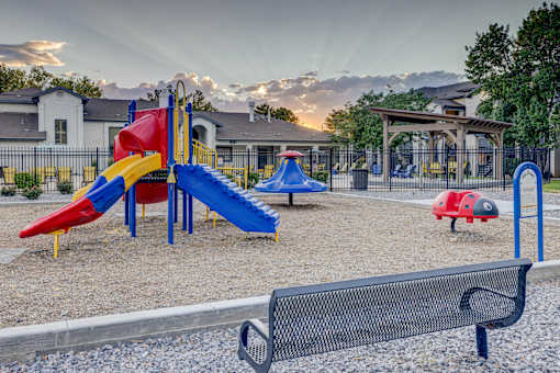 A playground with a red slide, blue slide, and a black bench.
