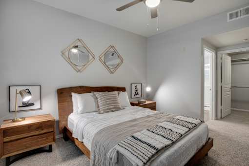 A bedroom with a bed, nightstand, and two mirrors on the wall.