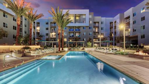 A swimming pool is surrounded by palm trees and lounge chairs at a resort.