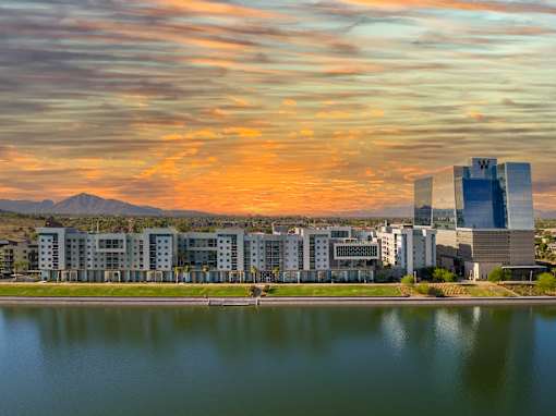 A serene landscape with a lake, buildings, and mountains under a vibrant sky.